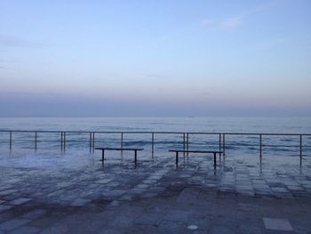 Empty benches on promenade by sea against sky