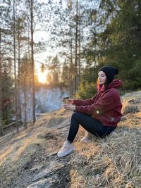 Young woman looking away while sitting on land in forest