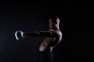 Side view of young woman exercising against black background