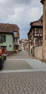 Footpath amidst houses in town against sky