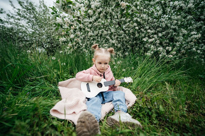 Little girl playing the ukulele in a blooming apple orchard in nature