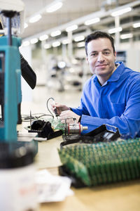 Portrait of mature male technician working on circuit board at desk in industry
