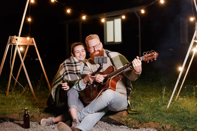 Woman recording with phone by man playing guitar at night