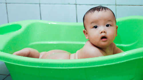 Cute wet baby in green plastic bathtub