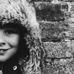 Cropped portrait of happy girl wearing fur jacket against brick wall