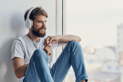 Man listening music while sitting by window at home