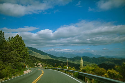 Empty road along trees and landscape against sky