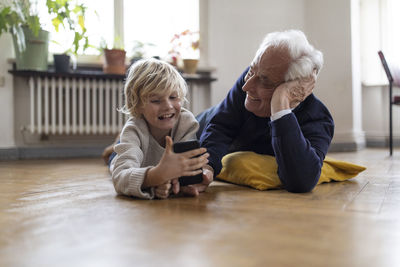 Grandfather and grandson lying on the floor at home using a smartphone