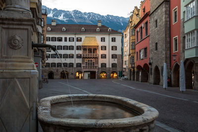 Fountain by street against buildings in city