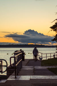 Man on railing by sea against sky during sunset