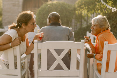 Retired senior women talking behind man while sitting at back yard