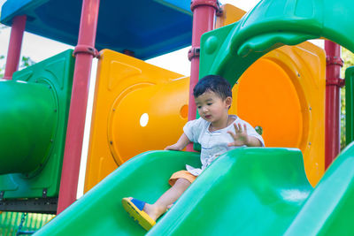 Full length of cute boy sitting on slide at playground