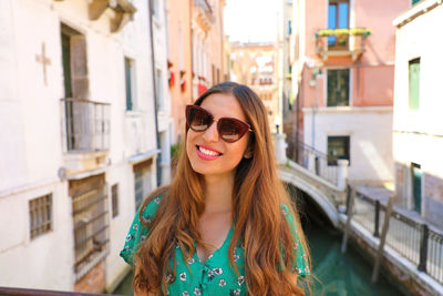 Portrait of smiling young woman standing against buildings