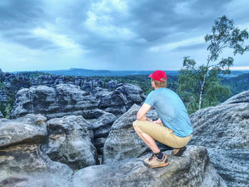 Man sitting on rock against sky