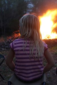 Rear view of girl sitting on stool against bonfire