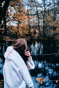 Rear view of woman standing by lake against trees