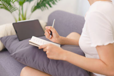 Midsection of woman using digital tablet while sitting on sofa at home