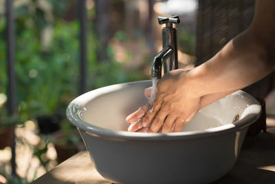 Close-up of hand holding faucet in bathroom