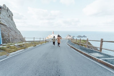 Rear view of man walking on road against sky