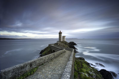 Lighthouse by sea against cloudy sky