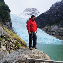 Man standing on rock looking at mountain against sky