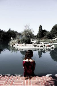 Rear view of woman standing by lake against clear sky