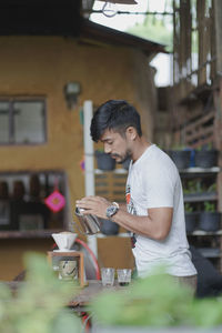 Side view of man pouring water while standing on table