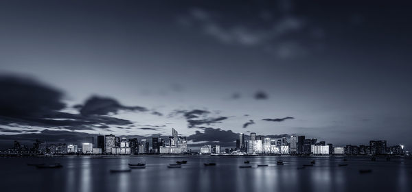 Illuminated cityscape by sea against sky at night