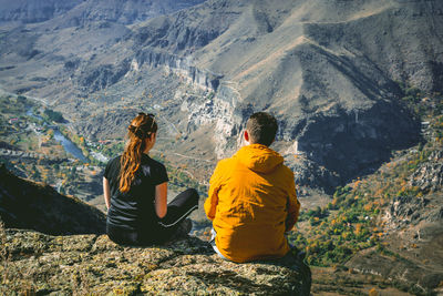 Rear view of couple sitting on cliff against mountains