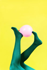 Low section of person holding pink balloon against yellow background