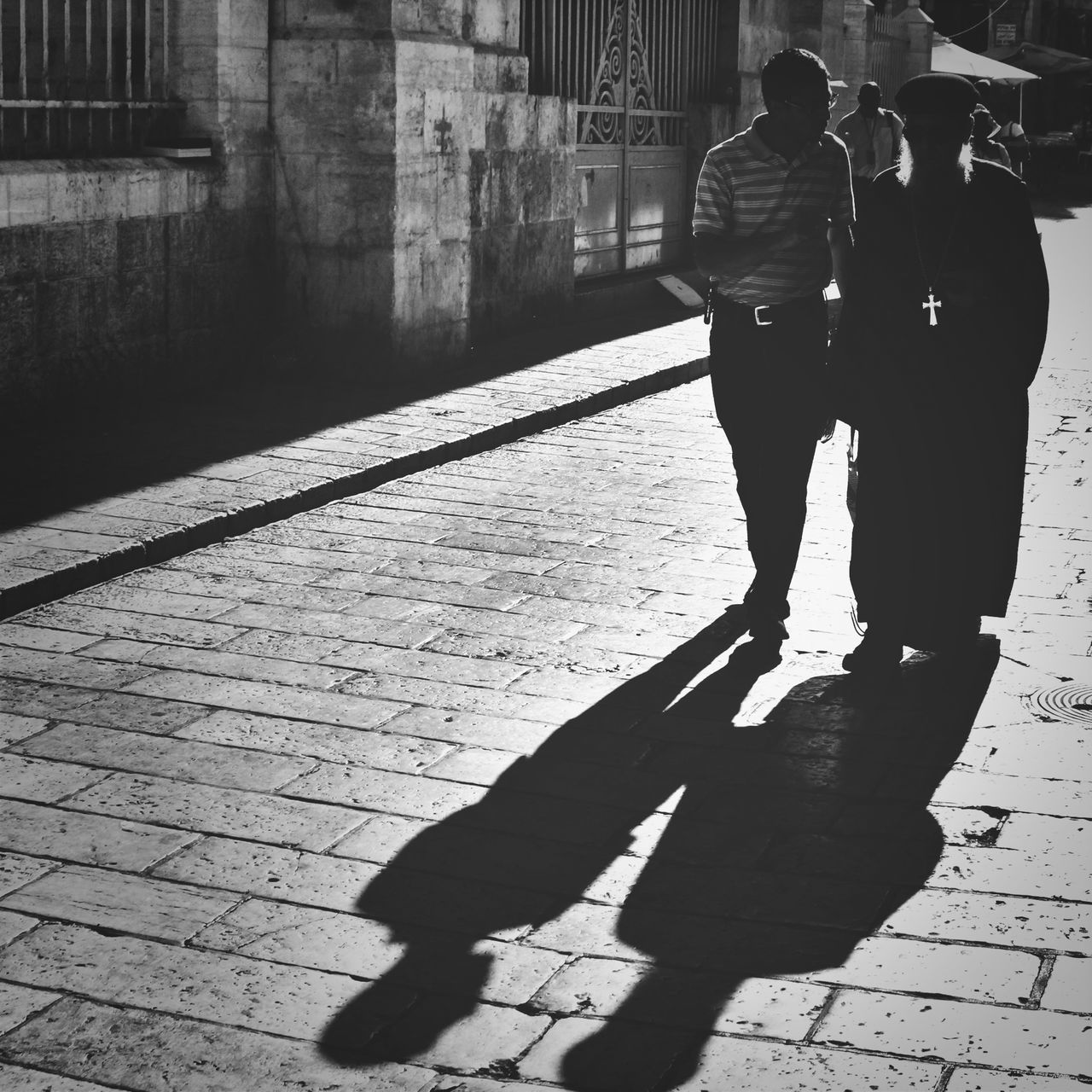 lifestyles, walking, street, men, shadow, leisure activity, full length, building exterior, sunlight, sidewalk, silhouette, person, built structure, city life, city, architecture, standing, rear view