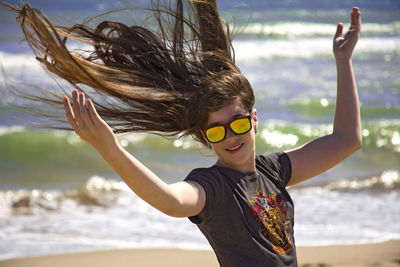 Woman hair blowing in wind at beach with arms raised on sunny day