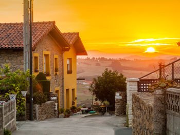 Houses by street amidst buildings against sky during sunset