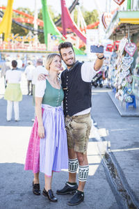 Smiling man and woman taking selfie while standing on street at event