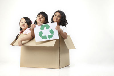Smiling girls holding sign while sitting box against white background