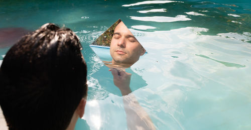 Reflection of man in mirror while sitting in swimming pool