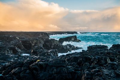 Rocks on shore against sky during sunset