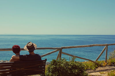 Rear view of women sitting on railing against sea