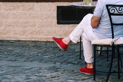 Low section of man wearing red shoe sitting on chair at sidewalk cafe