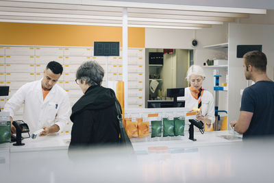 Rear view of customers buying medicines from pharmacists at checkout in store