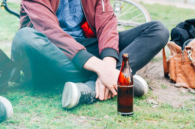 Low section of man sitting by bottle at grassy field