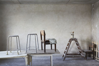 Empty chair and stools on floor against wall