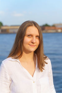 Portrait of cheerful young girl standing by river in city embankment, enjoing summer