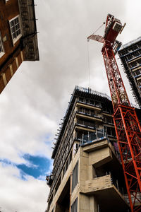 Low angle view of crane by building against sky