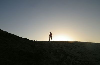 Silhouette man walking on desert against clear sky