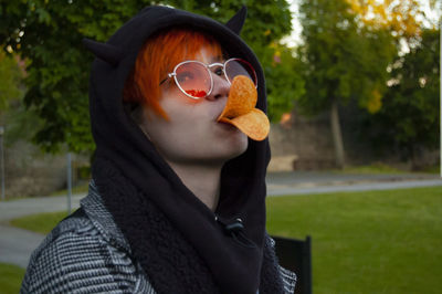 Young woman eating chips while wearing sunglasses in park