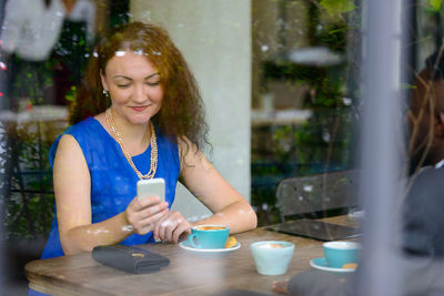 Smiling woman using mobile phone while sitting at cafe