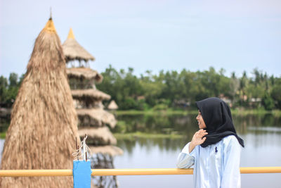 Side view of woman standing by railing and lake against sky