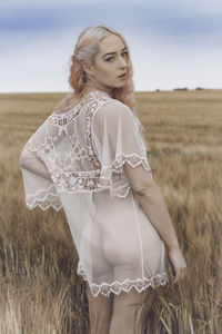 Rear view portrait of seductive young woman standing on field against sky