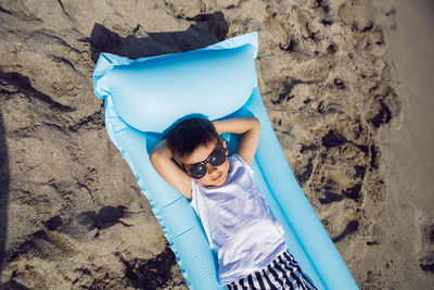 A child boy in sunglasses, a white t-shirt lies on an inflatable mattress on the seashore